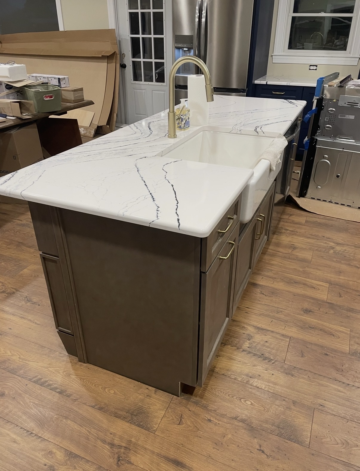 Marbled quartz island with farmhouse apron sink and brass gooseneck faucet