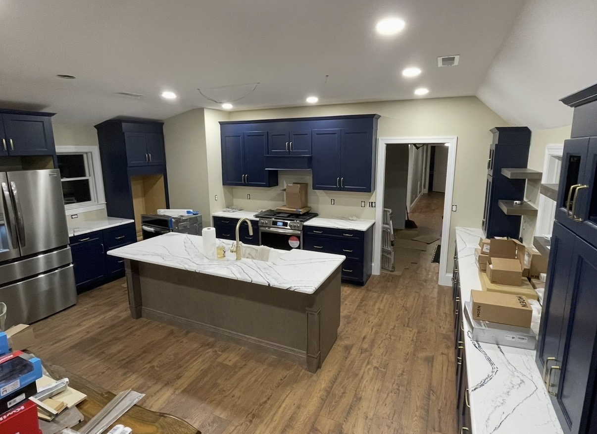 Wide view of completed navy shaker kitchen with marbled quartz island and stainless appliances