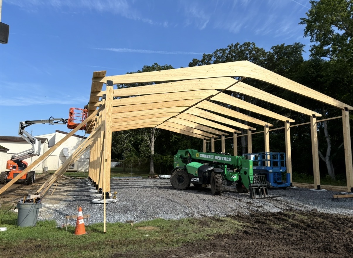Glulam roof beams partially raised over the timber post structure during the pavilion build